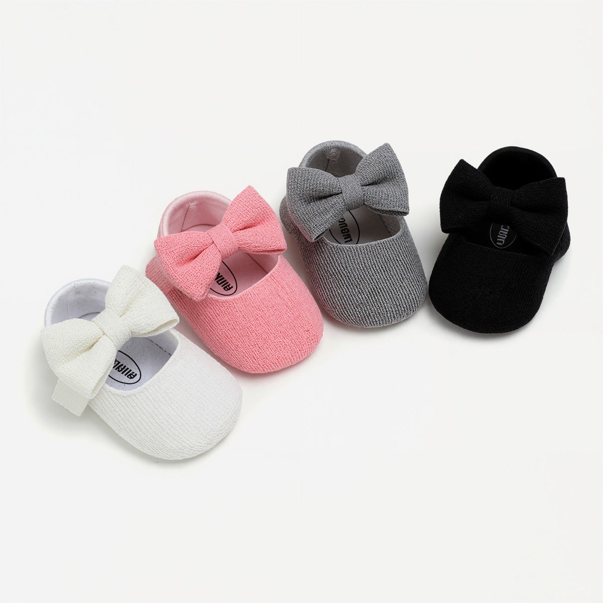 Four baby moccasin-style shoes with large bows, shown in white, pink, gray, and black on a clean white background.