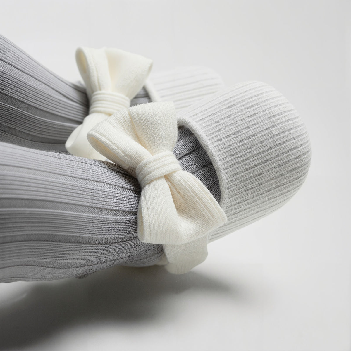 A close-up of a ribbed gray sock with a large cream-colored fabric bow tied around the top, photographed on a clean light gray background.