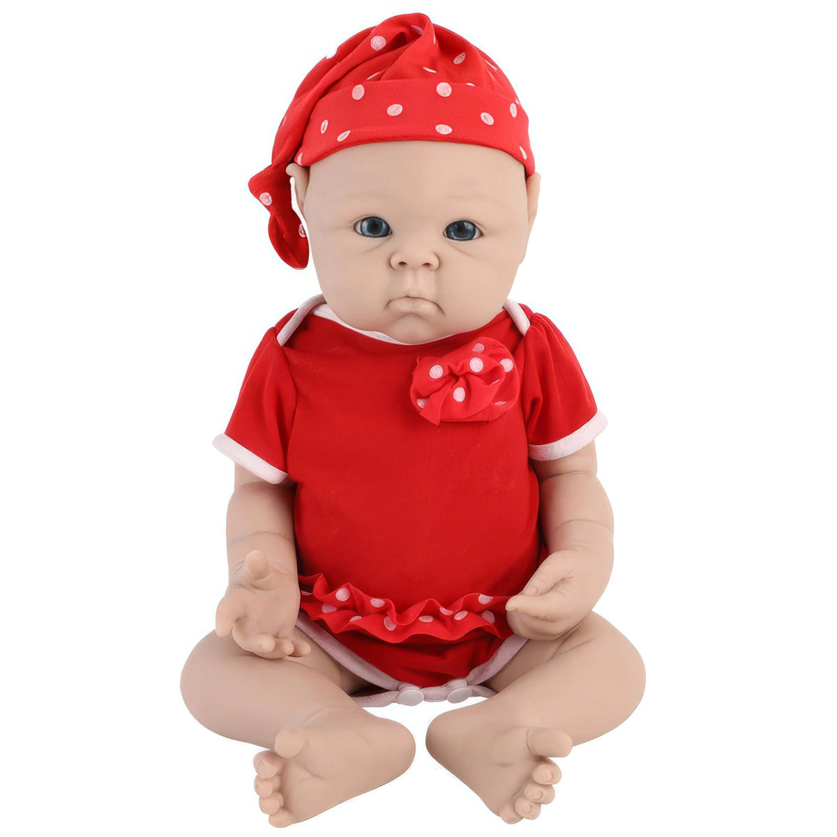 A realistic baby doll with a red short-sleeve romper and matching red polka-dot hat, seated against a plain white background.