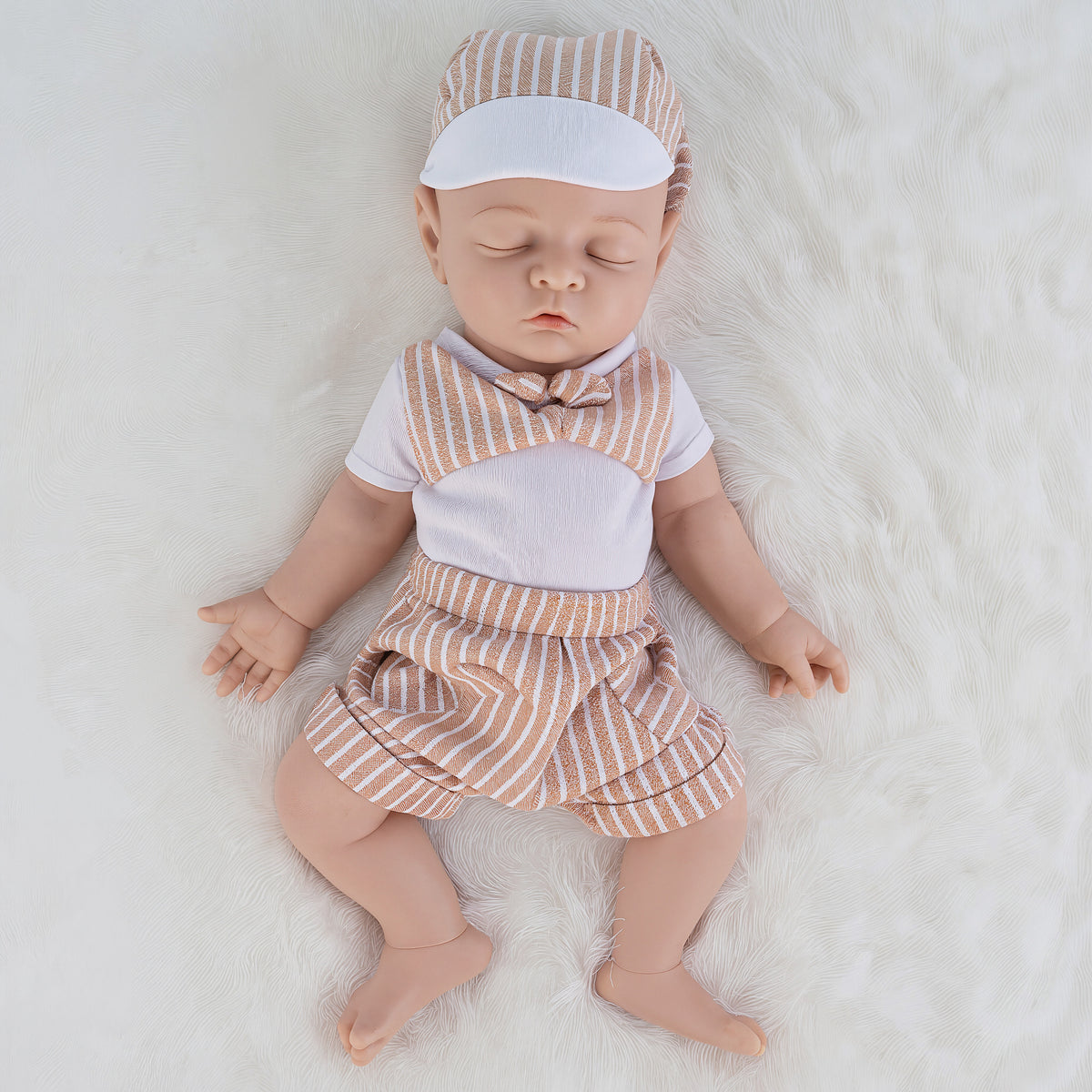A realistic baby doll or toy baby lying on a white faux fur surface, wearing a matching short-sleeve outfit and cap in beige and white vertical stripes with a solid white chest panel.