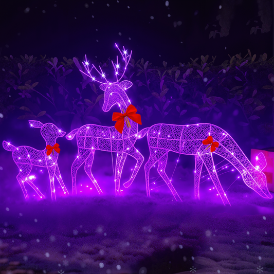 Three illuminated wire-frame deer sculptures in purple and pink with red bows, displayed outdoors at night in a snowy setting.