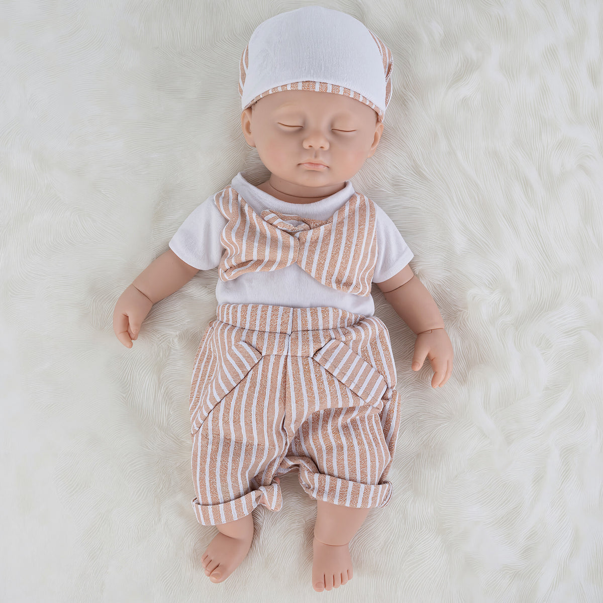 A baby doll dressed in a white short-sleeve shirt, peach-and-white vertically striped pants, and a matching striped bonnet, lying on a white faux-fur surface.