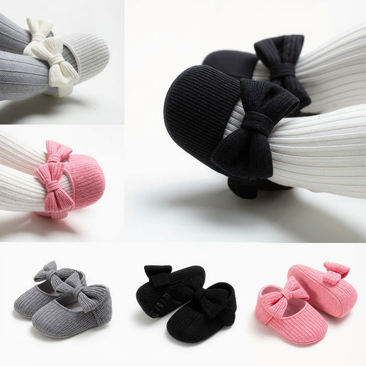 A collage showing baby booties with ribbed knit socks and large bows in multiple colors: white, black, pink, and gray. The main large view shows a black bootie with a black bow, while the smaller views show the other color options.